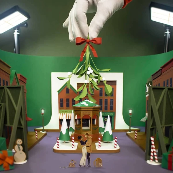Three-dimnesional illustration of a holiday movie set with a large hand holding the mistletoe above